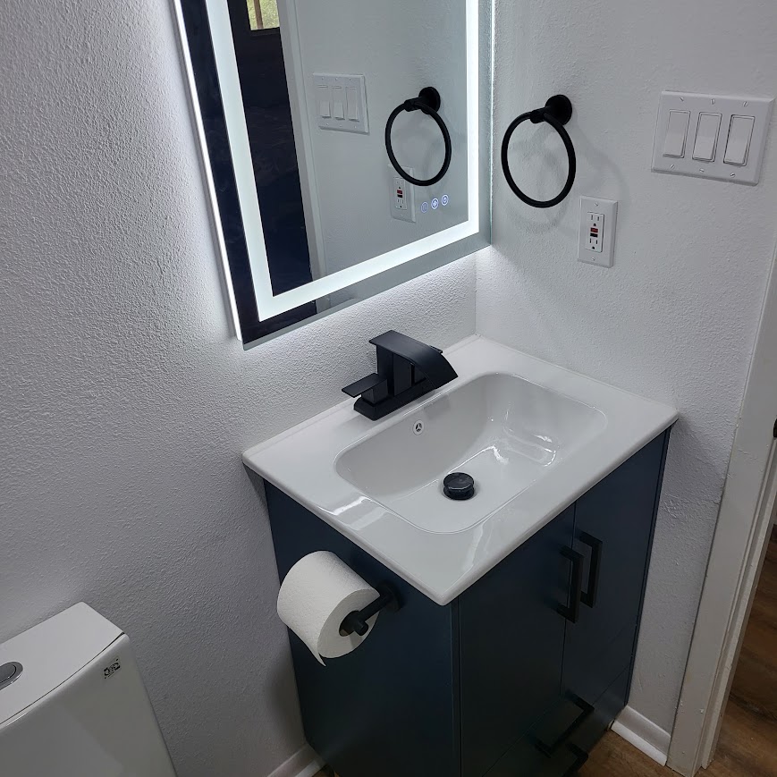 Navy vanity with backlit mirror and matte black fixtures, bathroom remodel