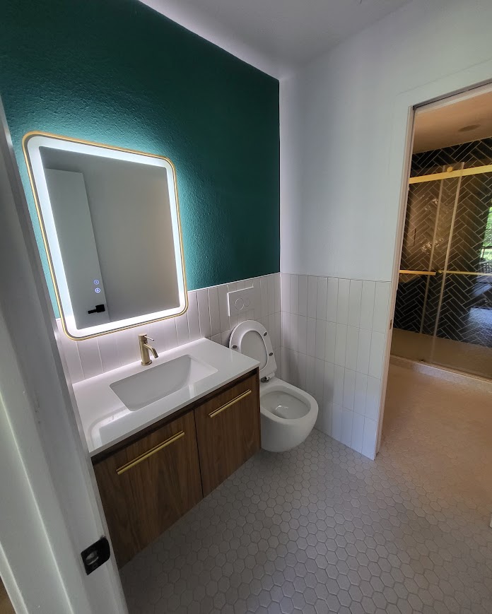 Teal accent wall with backlit round mirror and wood vanity, remodeled bathroom